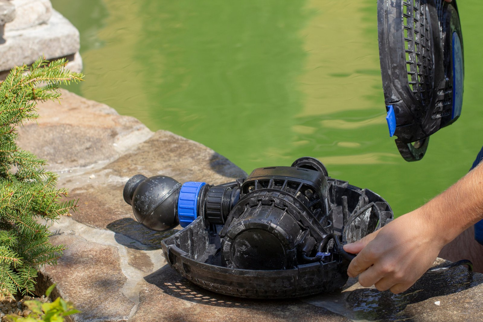 A water pump being handled on a stone surface near a green pond.