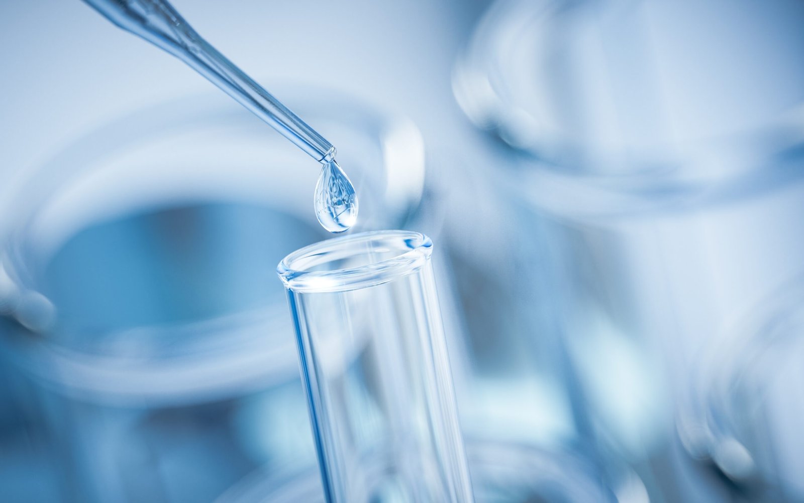 A clear pipette releasing a droplet into a glass test tube in a laboratory setting.