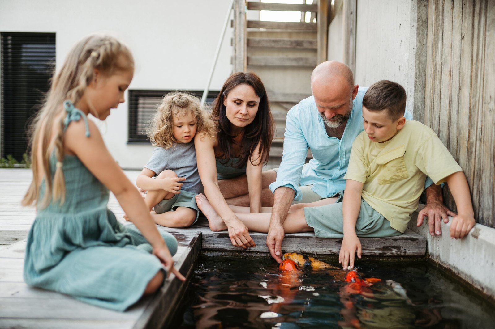 Family of four, including two children, interacting with koi fish in a water feature.