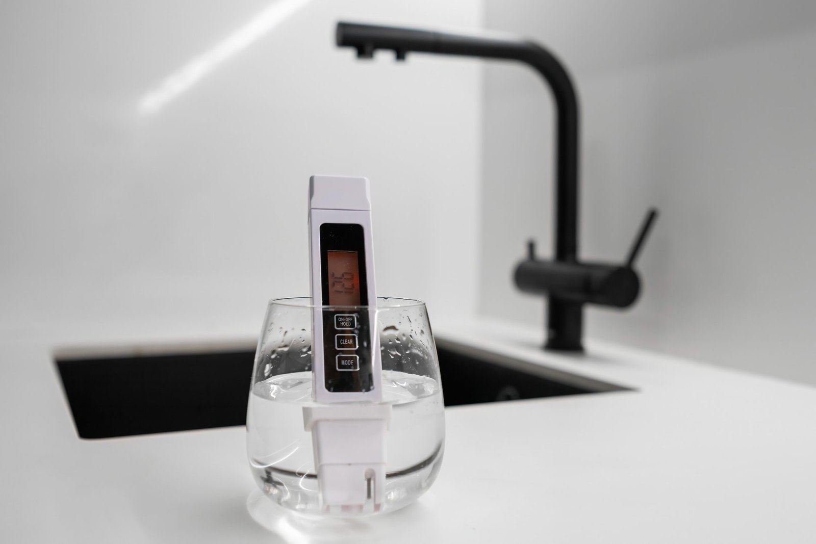 Digital water quality tester displaying temperature in a glass of water on a kitchen counter.