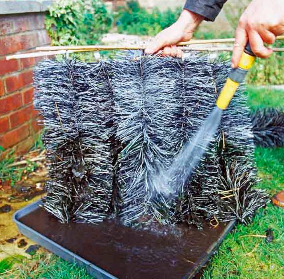 Person cleaning a set of brushes used for maintaining a water garden, with water spraying from a hose.