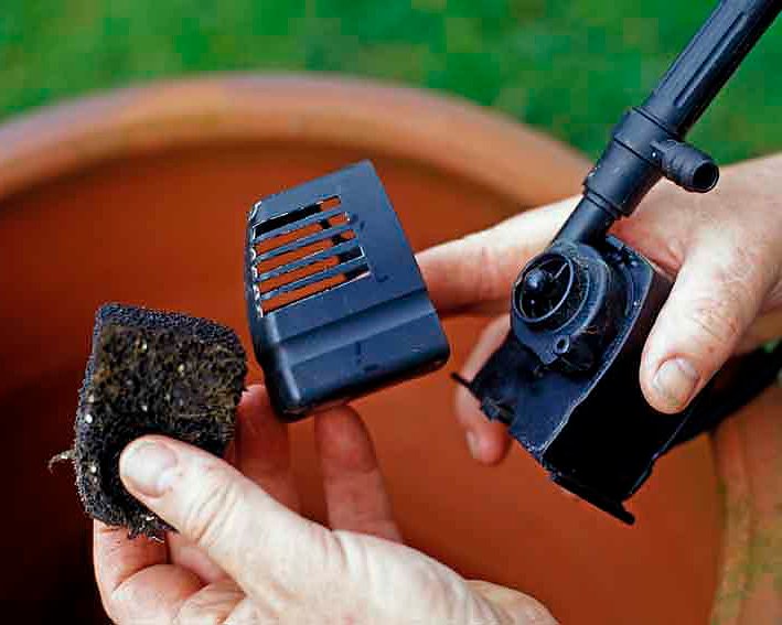 Hands holding a water pump component and filter sponge for a backyard water garden setup.