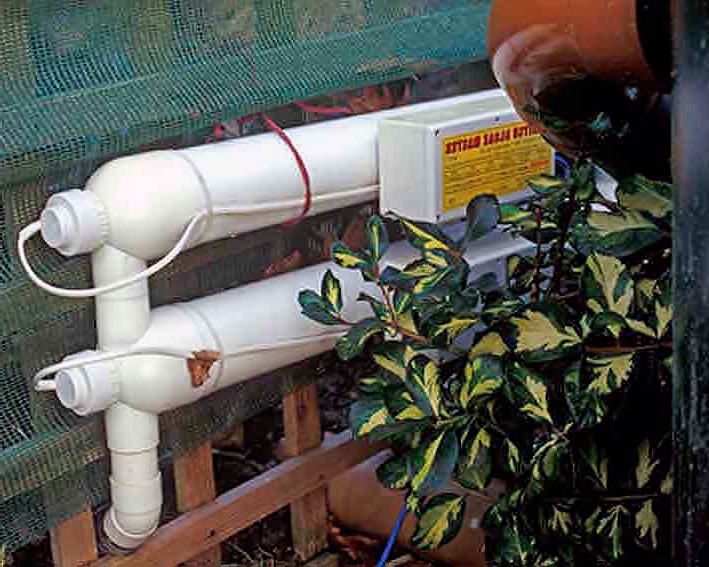A UV water clarifier unit with white pipes and a control box, positioned near a plant.