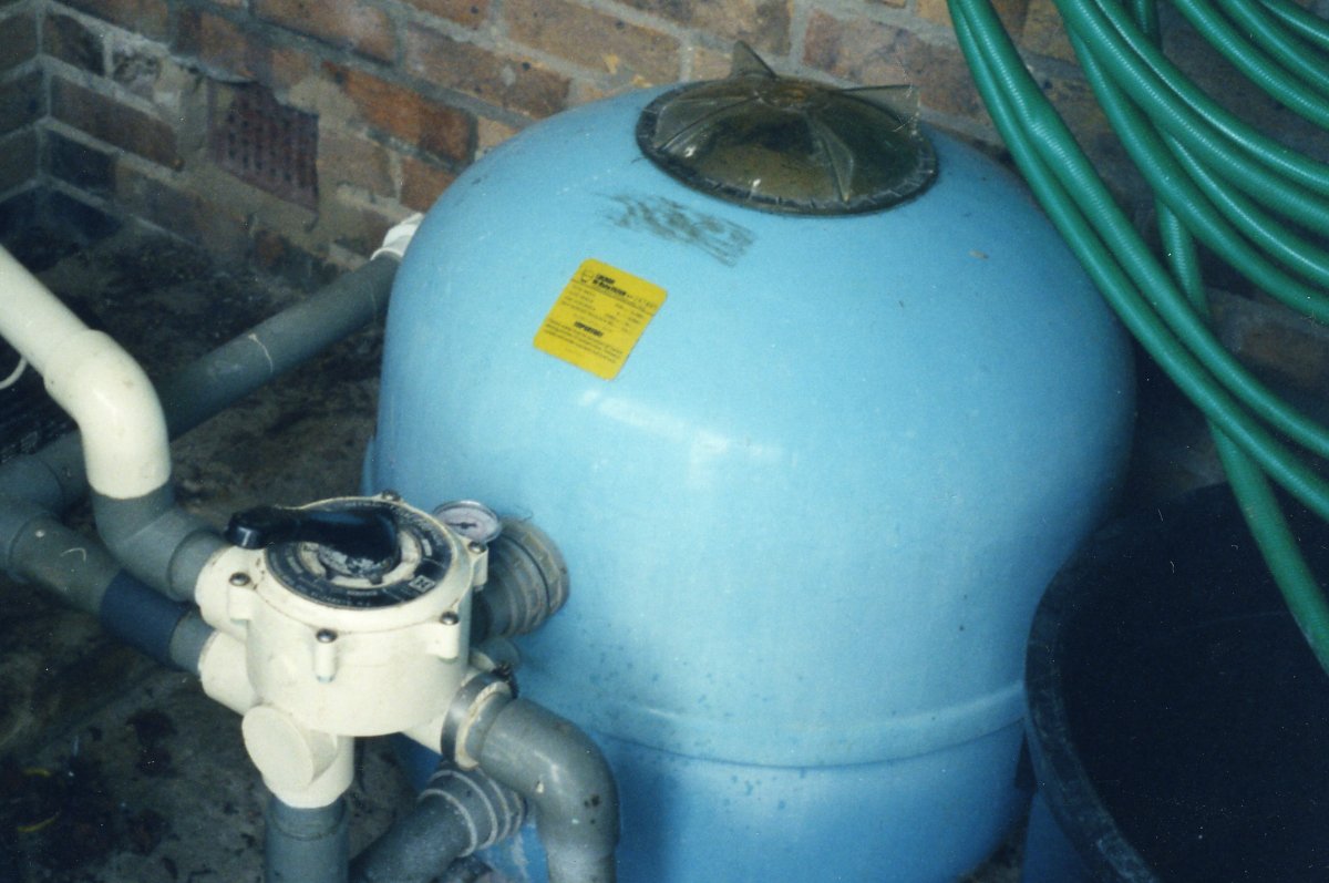 Blue external pressure filter with a white pump and gauge connected to it, situated in a garden setting.