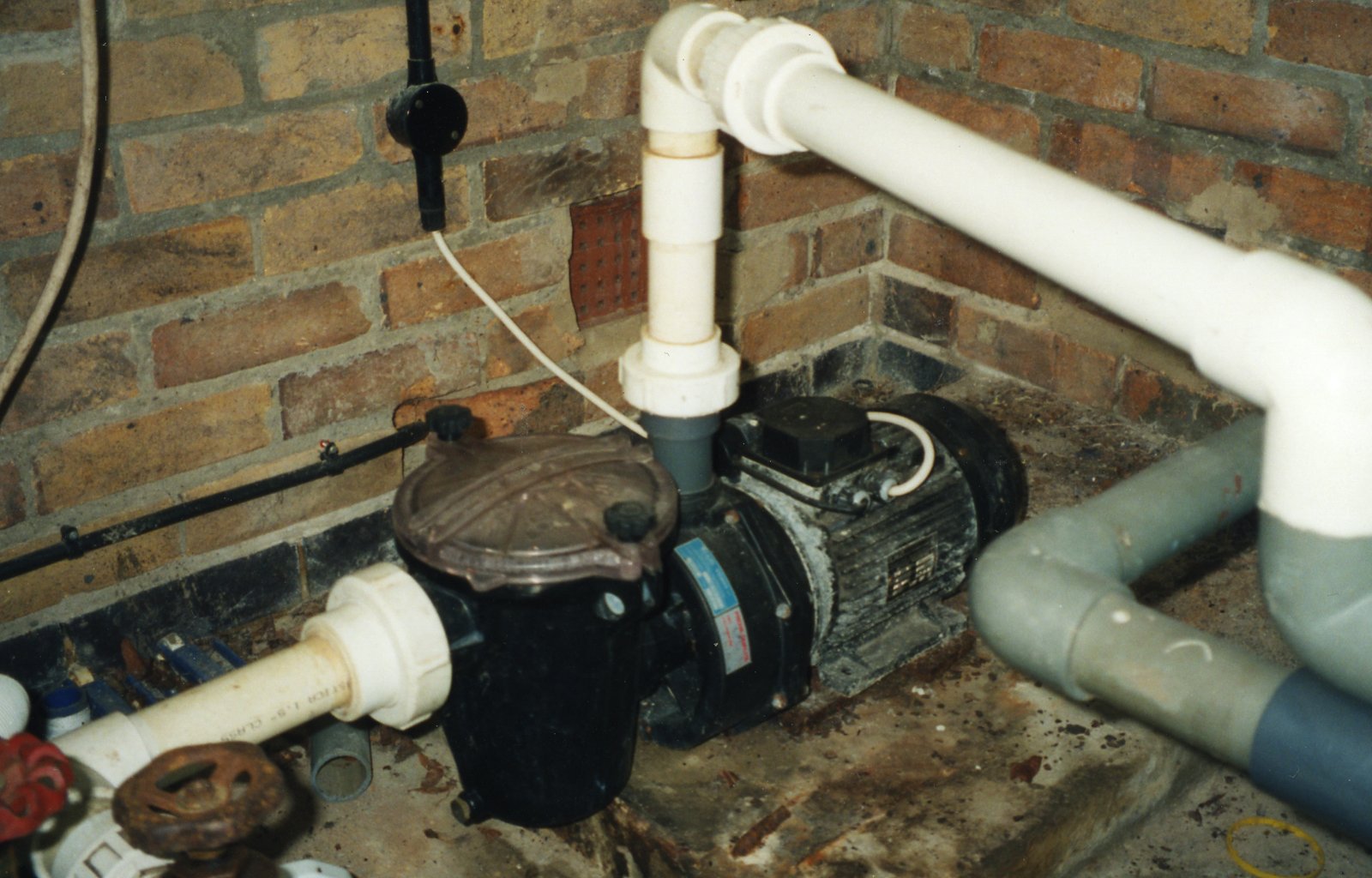External water pump with connected pipes in a basement setting, featuring a motor and various fittings.