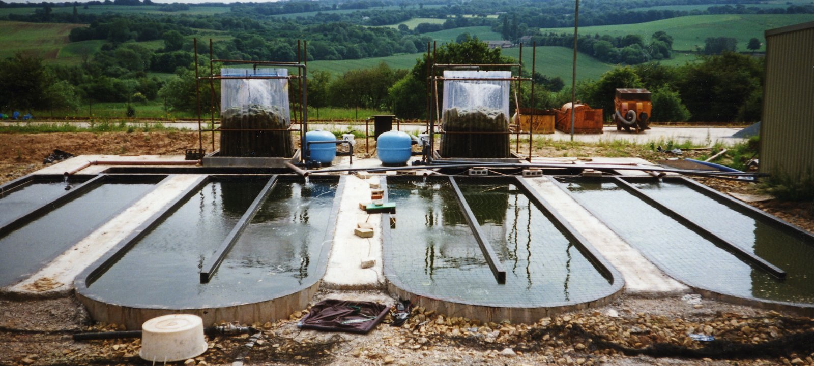 Two water treatment tanks with filtration systems and blue storage containers in an outdoor setting.