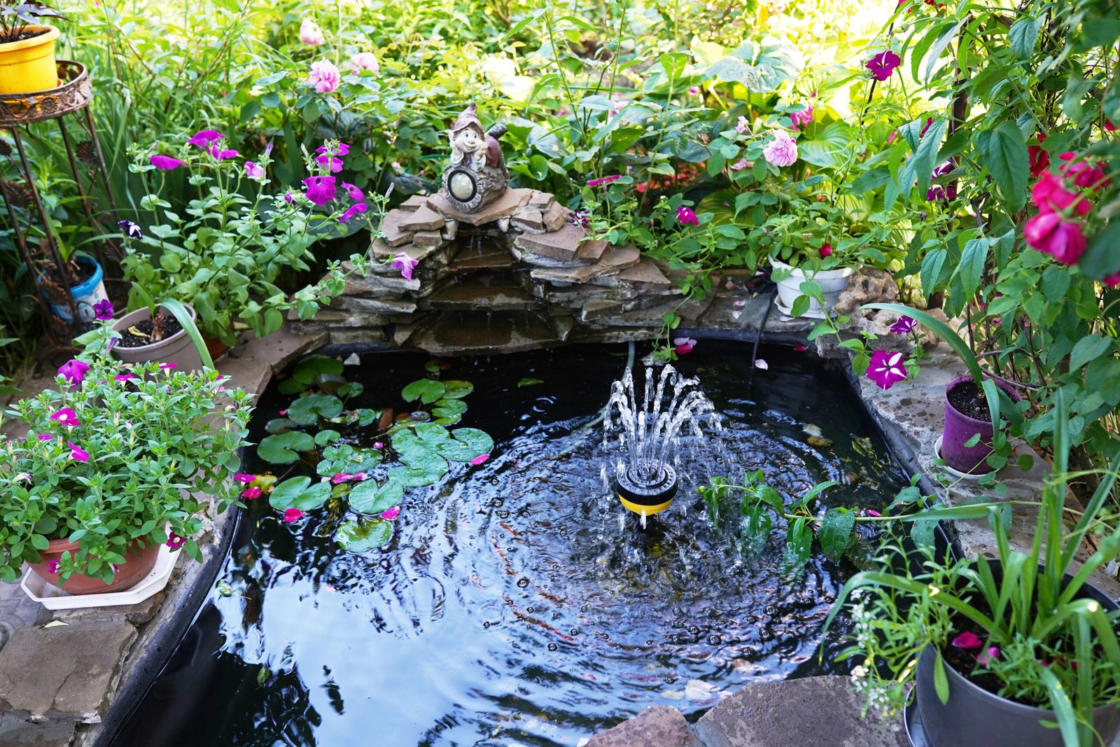 A tranquil backyard water garden featuring a small fountain surrounded by lush greenery and blooming flowers.