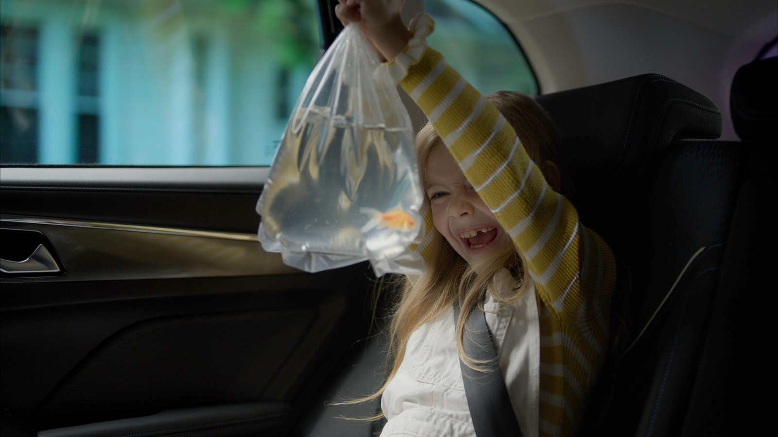 Young girl in a car holding a clear bag containing goldfish, smiling with excitement.