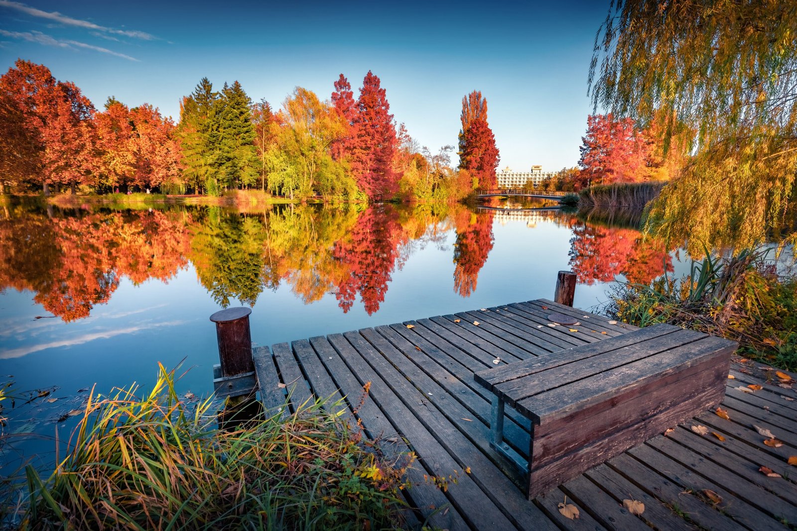 Wooden dock extending over a calm lake surrounded by trees with autumn foliage reflecting in the water.
