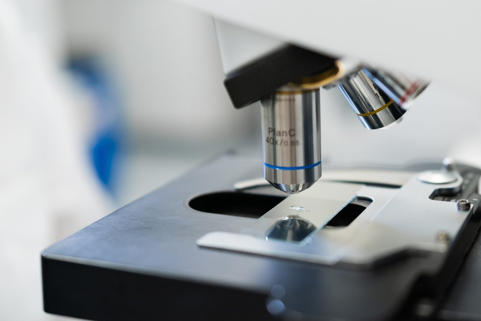 Close-up of a microscope objective lens positioned above a glass slide on a microscope stage.