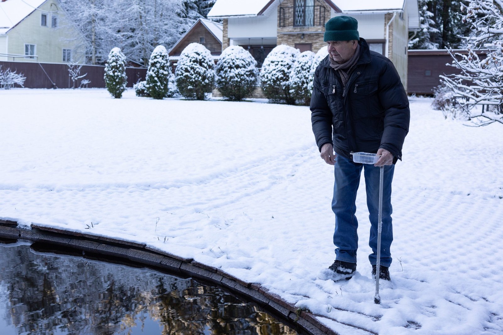 Man wearing a green beanie and jacket, standing on snow-covered ground beside a frozen pond.